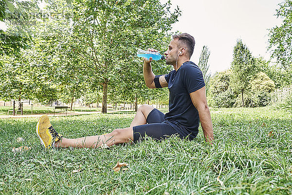 Mann trinkt nach dem Training ein Sportgetränk. Er befindet sich in einem Park im Freien.