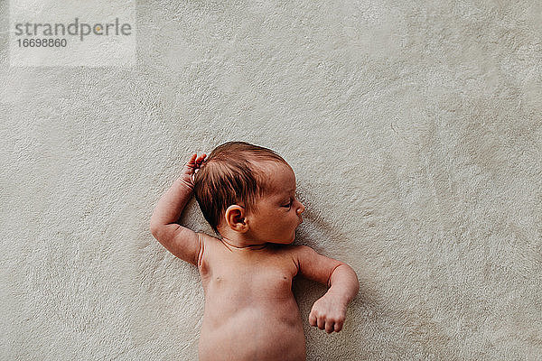 Neugeborenes Baby Arme  Bauch und Kopf auf einer weißen Decke liegend