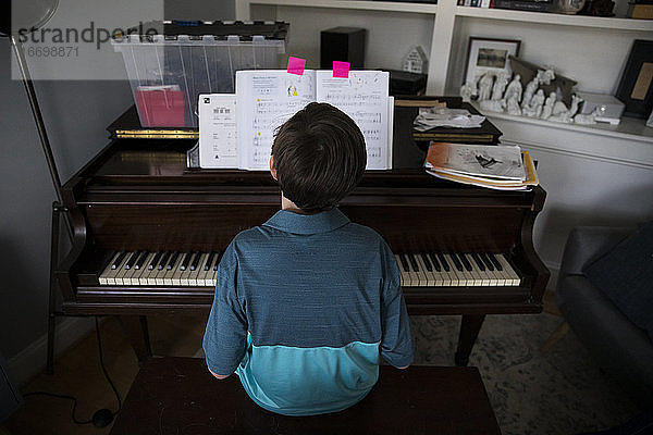 Rückansicht eines Tween Boy  der zu Hause Klavier spielt  von markierten Seiten im Buch