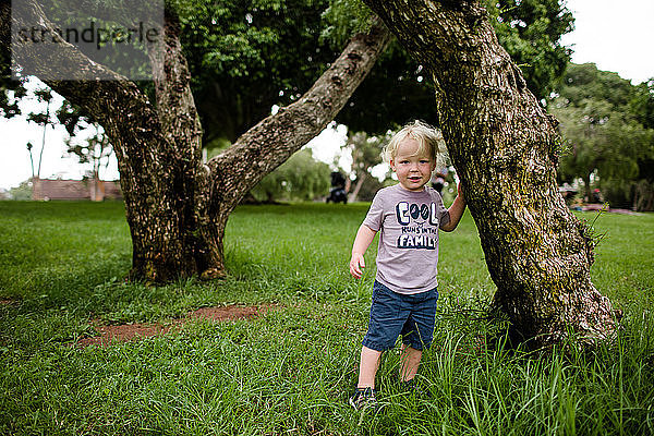 Zweijähriges Kind posiert neben einem Baum im Park