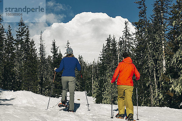 Zwei junge Frauen gehen an einem sonnigen Tag auf dem Mt. Hood Schneeschuhlaufen.