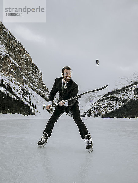 Mann in Anzug und Schlittschuhen jongliert Eishockey-Puck auf dem zugefrorenen Lake Louise