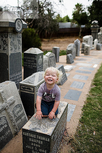 Zweijähriges Kind auf dem Grabstein sitzend und lächelnd