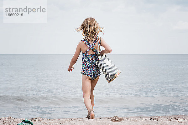 junges Mädchen mit einer Strandtasche in der Hand stolziert zum Meer
