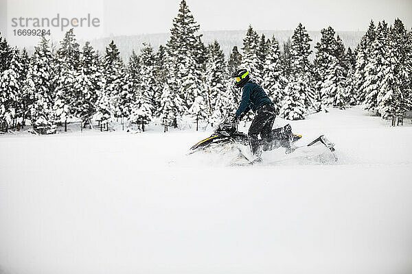 Seitenansicht eines Mannes beim Schneemobilfahren an einem verschneiten Tag.