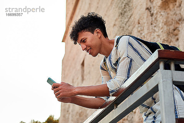 Junger Mann mit Afrohaar benutzt sein Smartphone im Freien