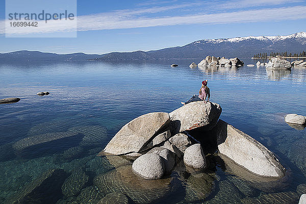 Frau betrachtet die Aussicht  während sie sich auf einem Felsen am Lake Tahoe an einem sonnigen Tag entspannt