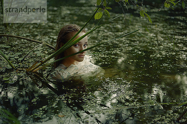 Eine Frau in einem weißen Kleid auf der Oberfläche eines Sumpfwassers im Wald