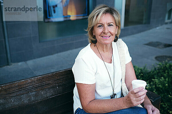 Dame auf der Bank sitzend  lächelnd bei einem Kaffee