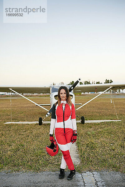 Junge Fallschirmspringerin auf einem Flugplatz mit einem Flugzeug hinter ihr