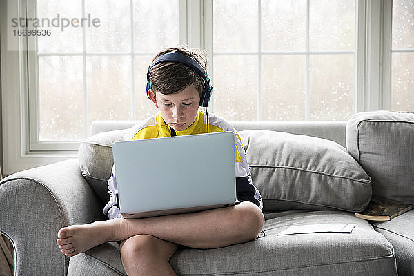 Junge im Teenageralter trägt Kopfhörer und arbeitet am Laptop für die virtuelle Schule