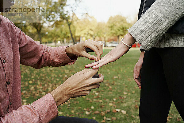 Kniender Mann  der seiner Freundin mit einem Ring in einem Park die Ehe anbietet. Liebe Konzept