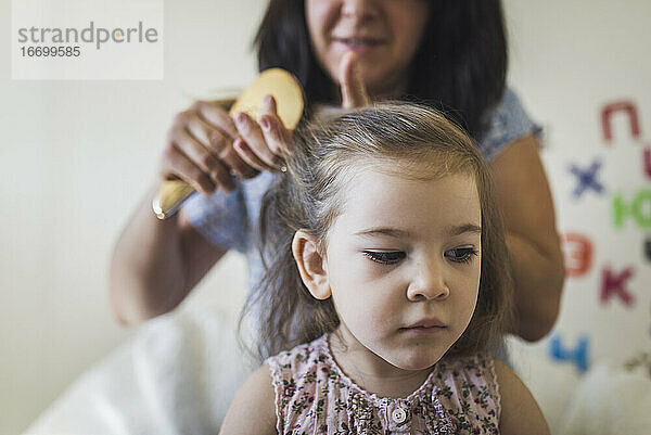 Mama bürstet die Haare ihrer ernsten 4 Jahre alten Tochter