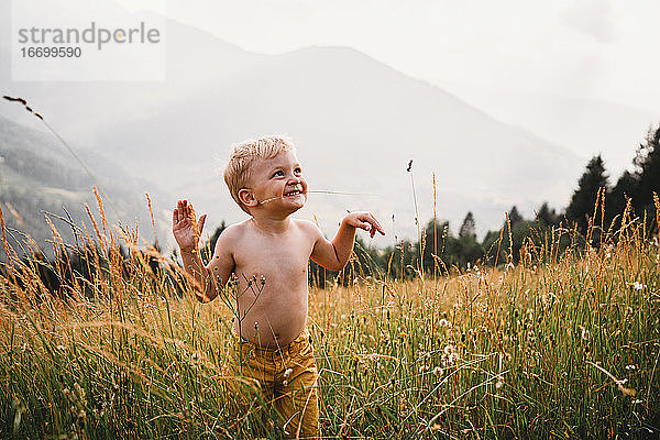 Kind mit Gras im Mund lächelnd in den Alpen