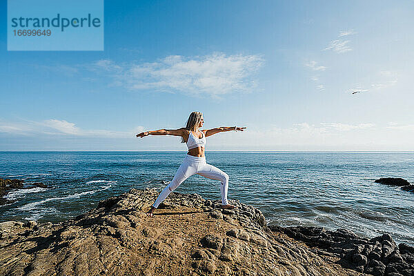 Junge Frau macht Yoga-Übungen am felsigen Strand