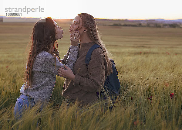 zwei Frauen halten sich bei Sonnenuntergang auf einem Feld an den Händen