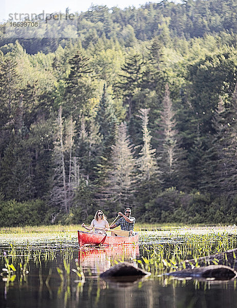 Paar  weiße Frau und schwarzer Mann  paddeln in rotem Kanu auf einem See  Maine