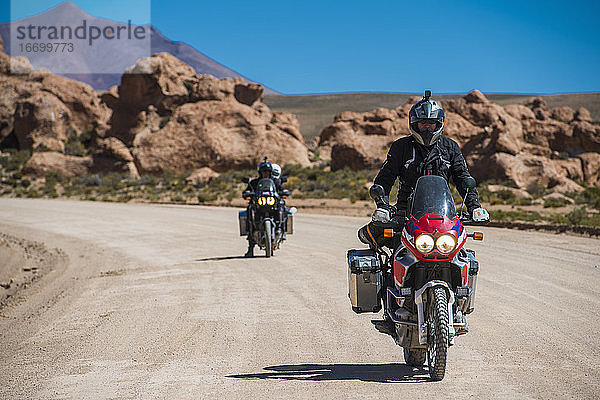 Zwei Freunde fahren auf einem Tourenmotorrad auf einer staubigen Straße in Bolivien