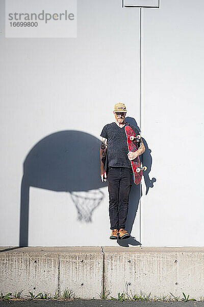 Porträt eines erwachsenen Mannes  der ein Skateboard in hellem Sonnenlicht hält