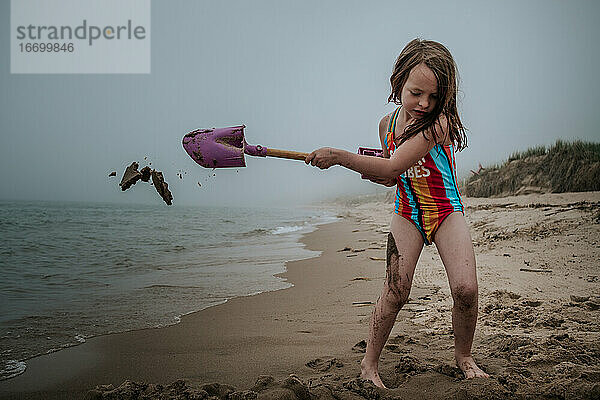 junges Mädchen gräbt in Sand am Strand an einem bewölkten Tag