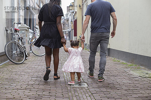 Ein junges Paar geht mit seiner Tochter auf europäischen Straßen spazieren