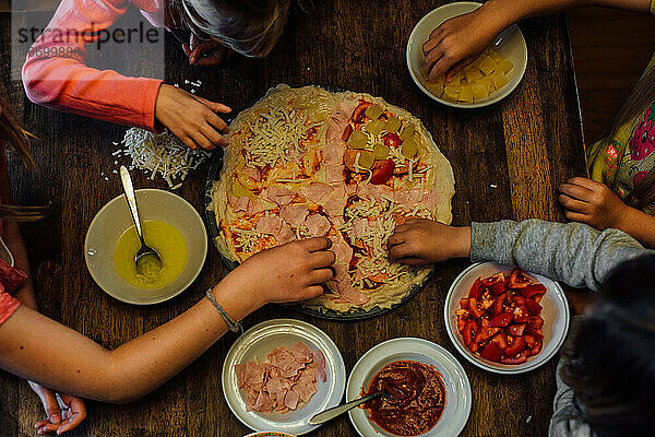 Kinder  die gemeinsam am Tisch eine selbstgemachte Pizza essen