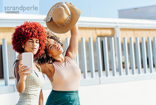 Zwei attraktive Latino-Mädchen mit Afro-Haar nehmen ein Selfie mit Telefon.