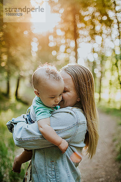 Vertikale von glücklichen Mutter kuscheln Baby Junge draußen im Wald