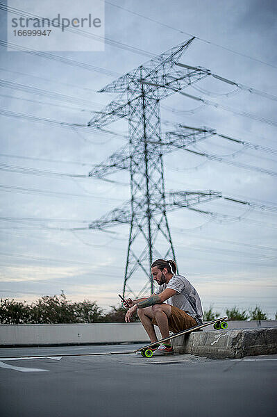 Junge posiert mit Skateboard in der Hand und Telefon