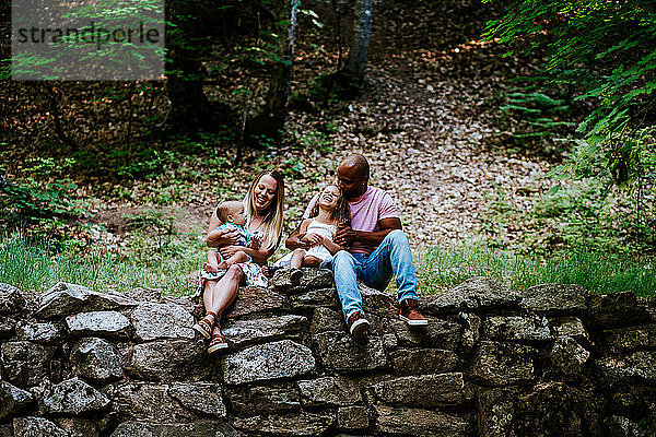 Glückliche gemischtrassige Familie  die lachend auf Felsen im Wald sitzt