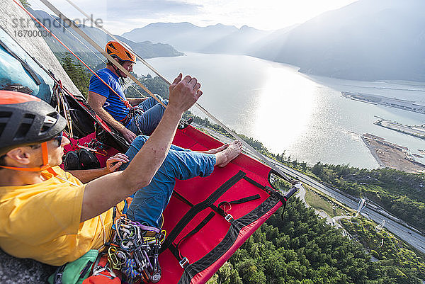 Zwei Männer sitzen auf einem Portaledge und genießen den Sonnenuntergang und die Aussicht in Squamish