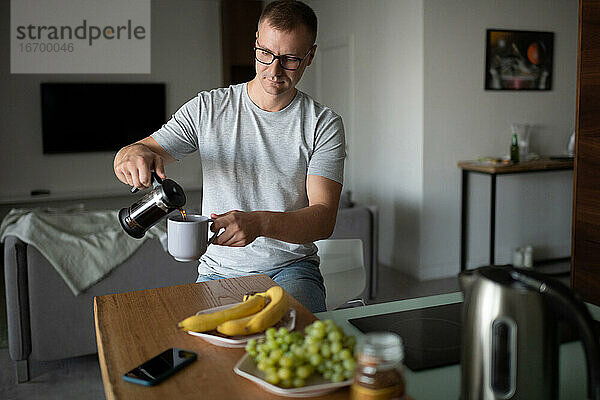 Erwachsener Mann gießt morgens Tee ein