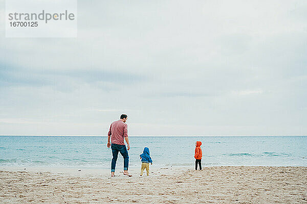 Vater und Kinder am Strand an einem bewölkten und kalten Tag