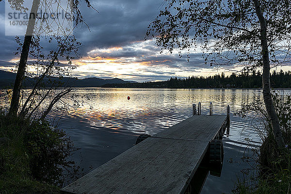 Dock mit Leiter durch ruhigen See während Sonnenaufgang mit Reflexion der Wolken