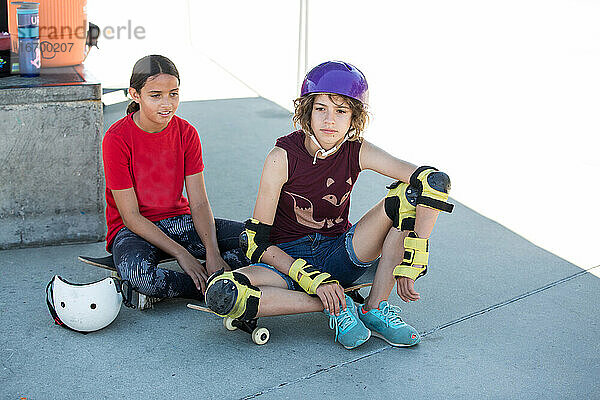 Zwei Mädchen sitzen mit ihren Skateboards auf dem Skatepark im Schatten