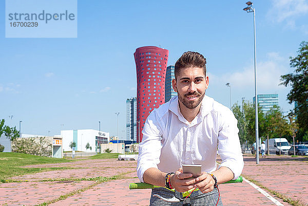 Outdoor-Porträt eines gut aussehenden jungen Mannes mit Mobiltelefon und Fahrrad mit festem Gang auf der Straße.