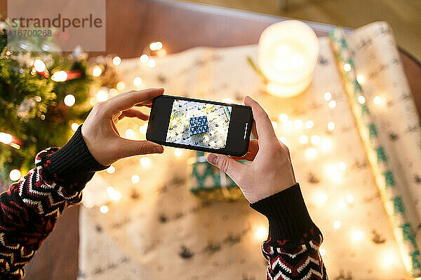 Mann fotografiert mit Smartphone sorgfältig verpacktes Weihnachtsgeschenk