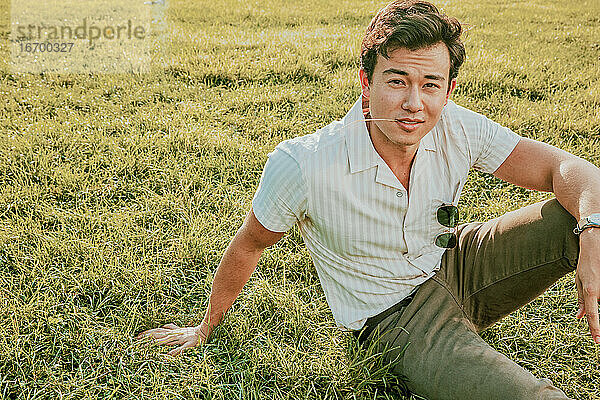 Porträt eines jungen Mannes  der im Gras sitzt.