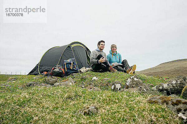 Glückliches Paar mit Buch beim Zelten in den Hügeln