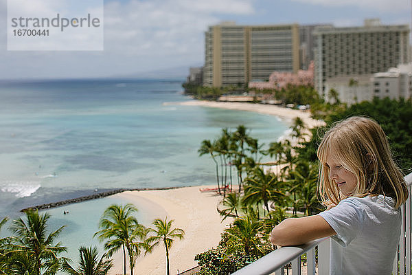 Lächelndes Mädchen genießt die Aussicht auf den Ozean von Waikiki vom Hotelbalkon aus (Tilt-Shift)