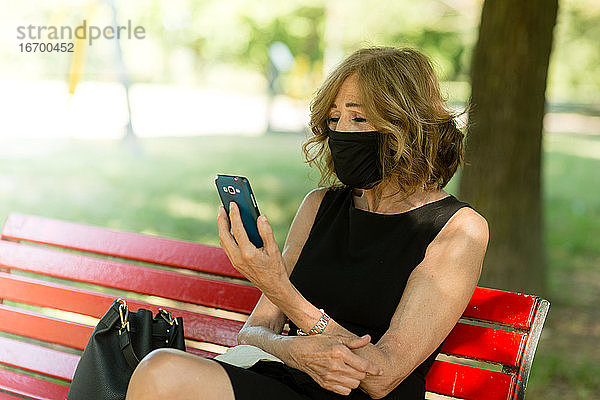Porträt einer attraktiven eleganten älteren Frau mit Maske am Telefon