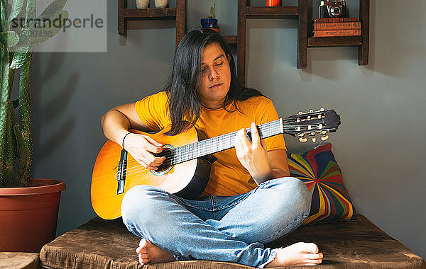 Mann mit langen Haaren  der während der Quarantäne zu Hause entspannt Gitarre spielt