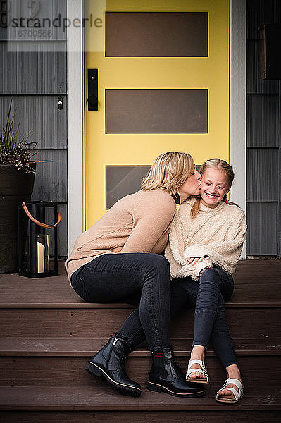 Mutter küsst Tochter auf Stufen vor einer gelben Tür