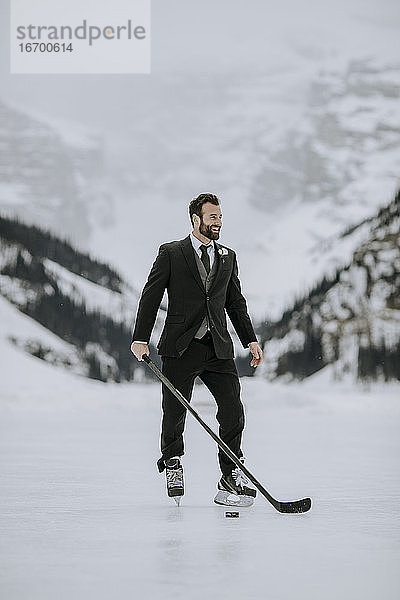 Mann in schwarzem Anzug  Hockey-Schlittschuhen und Hockeyschläger posiert auf zugefrorenem See