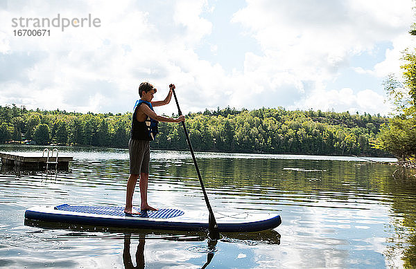 Ein Jugendlicher paddelt auf einem SUP auf einem See in Ontario  Kanada  an einem sonnigen Tag.