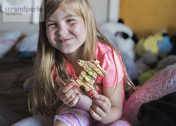 Junges Mädchen lächelt und isst einen Lebkuchenmann in ihrem Schlafzimmer