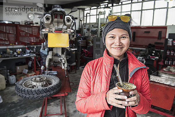 Porträt einer Frau  die in einer Motorradmechanikerwerkstatt Mate-Tee trinkt