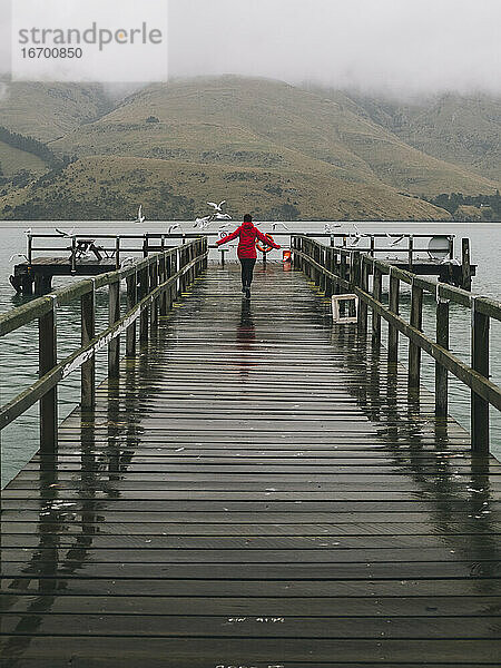 Frau in roter Jacke läuft fröhlich am Port Levy Jetty  NZ