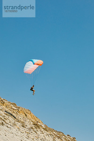 Junger Mann beim Gleitschirmfliegen im Sommer von den Klippen in Baja  Mexiko.