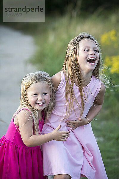 Lachende junge Schwestern in rosa Sommerkleidern